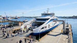 Un grande traghetto elettrico moderno attraccato in un porto trafficato, con infrastrutture di ricarica ben visibili. (Immagine generata con IA)