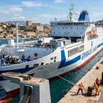 Traghetto Ro-Pax di Grimaldi Lines in fase di attracco in un porto trafficato, con membri dell'equipaggio e operatori portuali. (Immagine generata con IA)