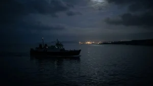 Immagine suggestiva di un traghetto in lontananza nella notte, con luci portuali sullo sfondo, evocativa della memoria del disastro Moby Prince e della ricerca della verità. (Immagine generata con IA)